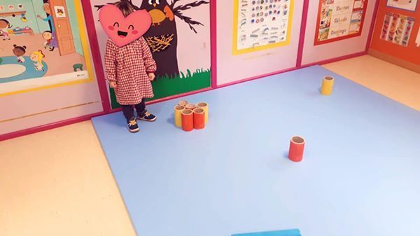 Una niña que lleva una máscara de corazón está parada sobre una alfombra azul en una habitación.