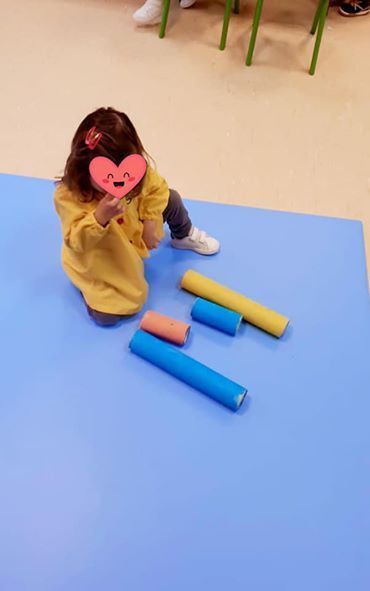 Una niña está sentada en el suelo sosteniendo un corazón frente a su cara.