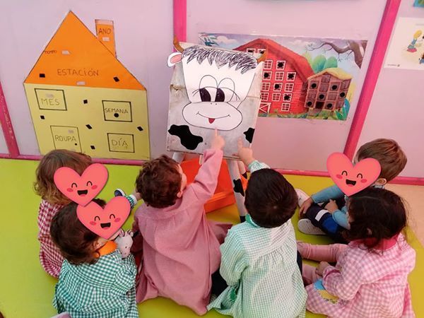 Un grupo de niños está sentado en el suelo jugando con una marioneta de vaca.