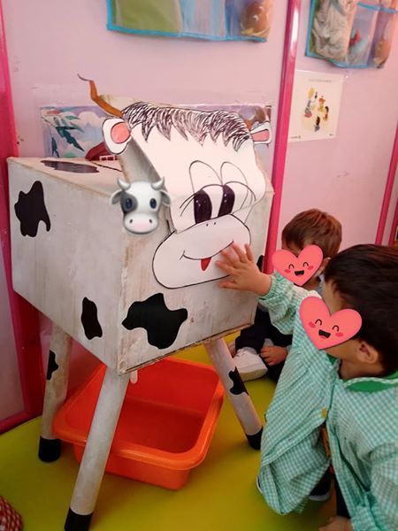 Los niños están jugando con una vaca hecha con una caja de cartón.