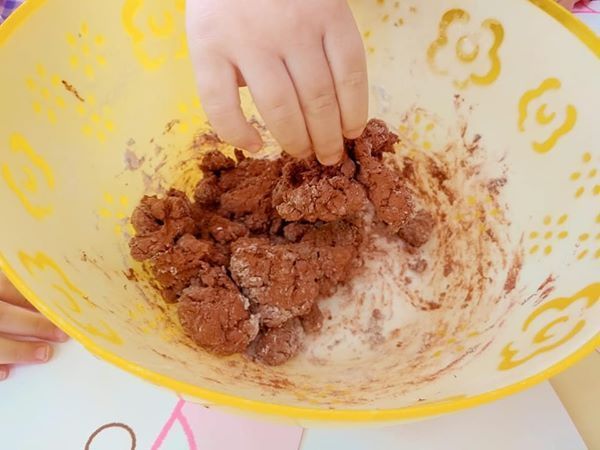 Un niño está jugando con arcilla en un recipiente amarillo.
