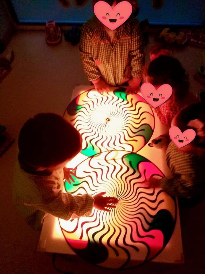 Un grupo de niños está sentado alrededor de una mesa jugando con una caja de luz.