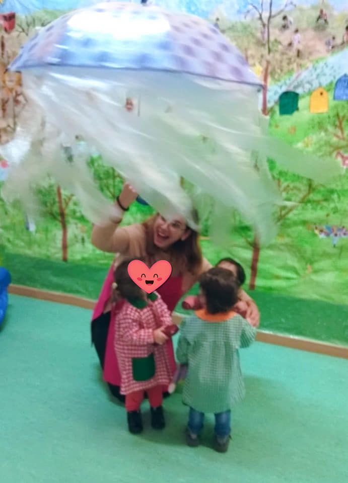 Una mujer sostiene un paraguas con forma de medusa sobre dos niños.