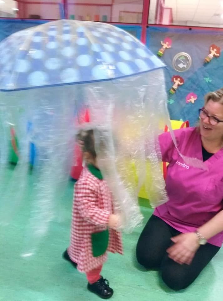 Una mujer con un uniforme rosa está arrodillada junto a una niña que sostiene una medusa inflable.