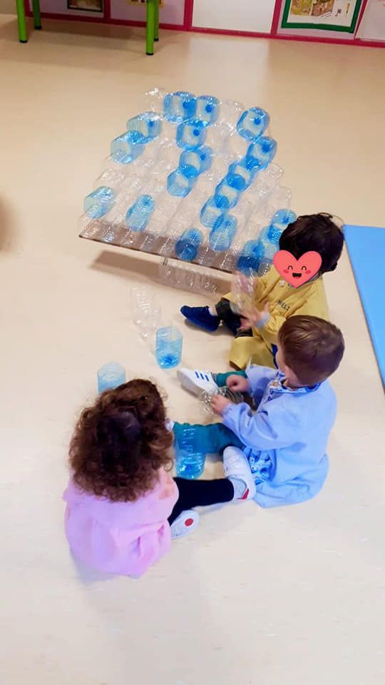 Tres niños están sentados en el suelo jugando con botellas de plástico.