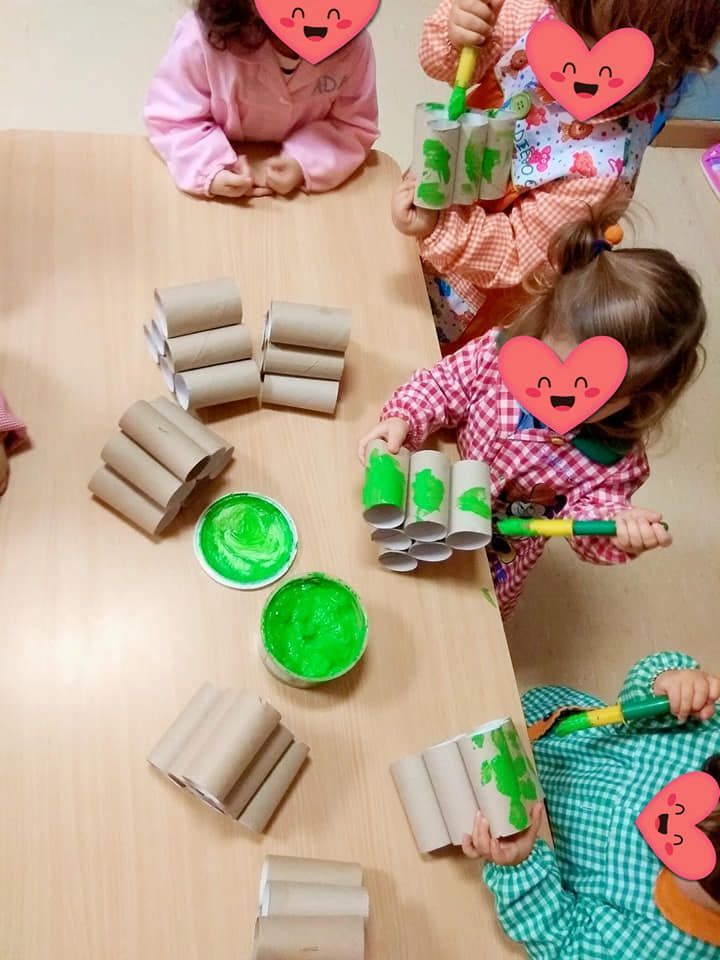 Un grupo de niños está sentado en una mesa jugando con rollos de papel higiénico.