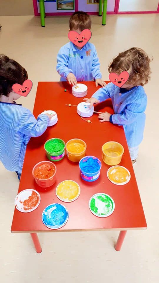 Un grupo de niños está jugando con pintura en una mesa roja.