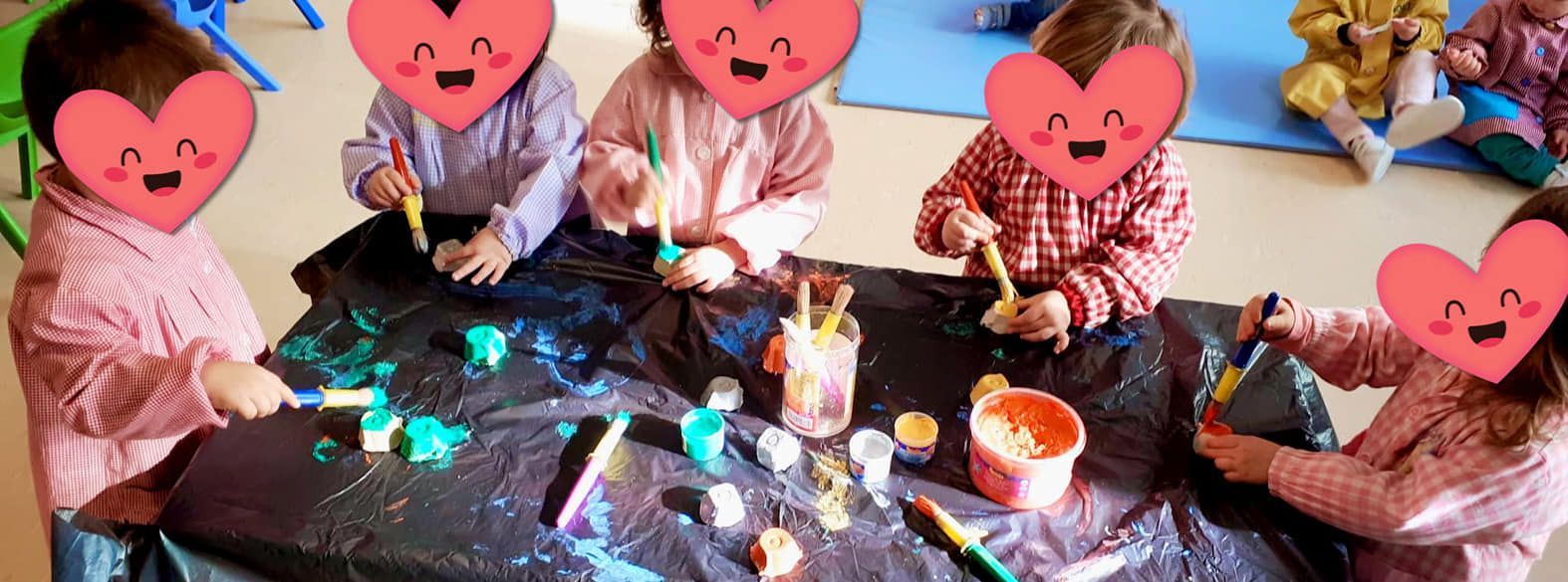 Un grupo de niños están sentados alrededor de una mesa pintando.