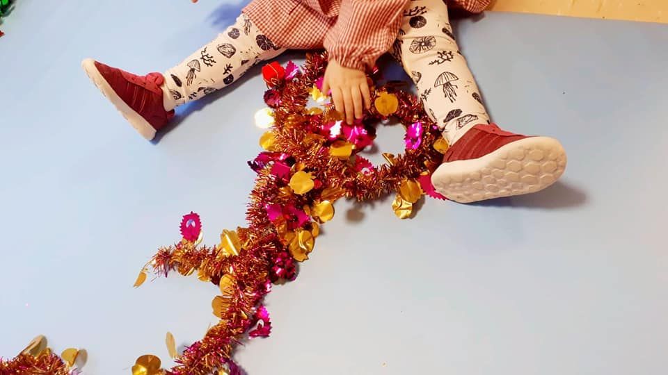 Una niña está sentada en el suelo jugando con oropel.