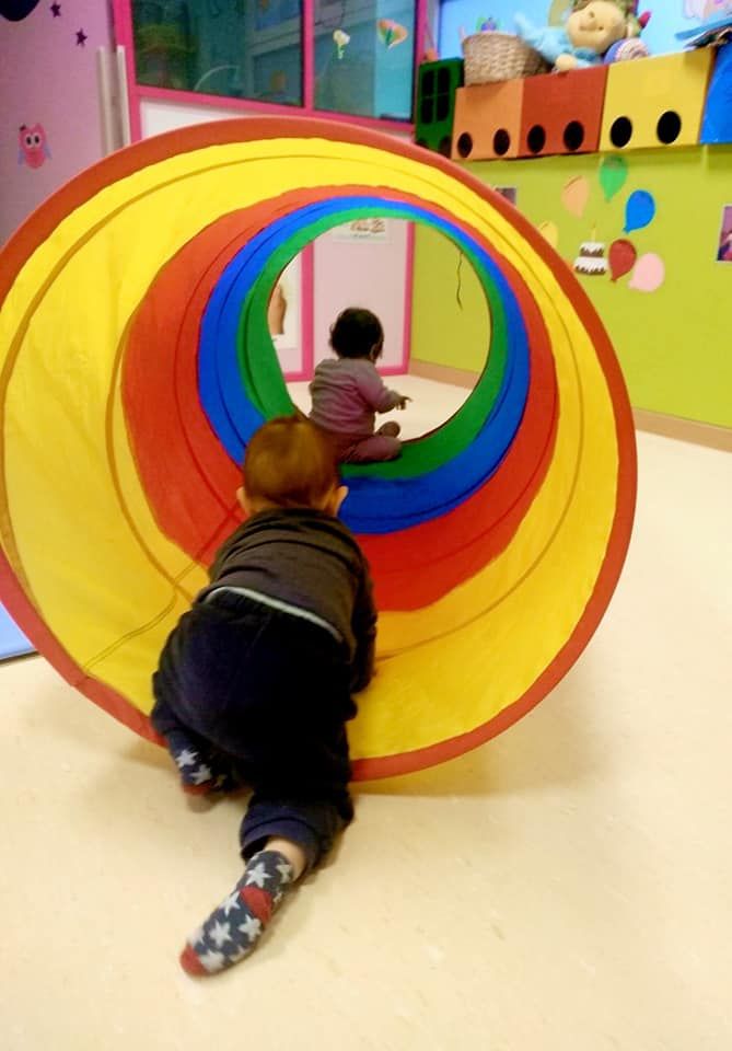 Dos niños gatean por un túnel colorido.