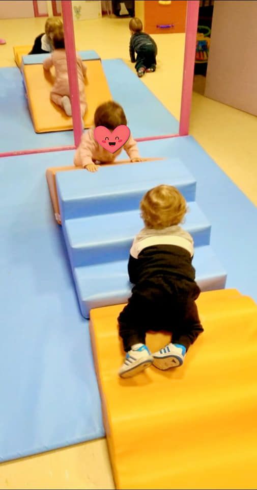 Un bebé gatea sobre una alfombra amarilla frente a un espejo.