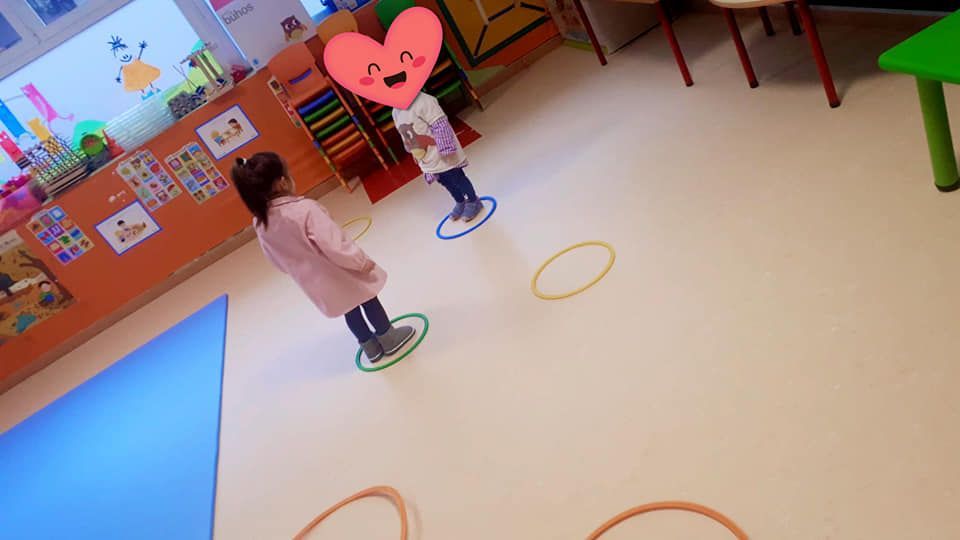 Dos niñas juegan con aros de hula hula en un aula.