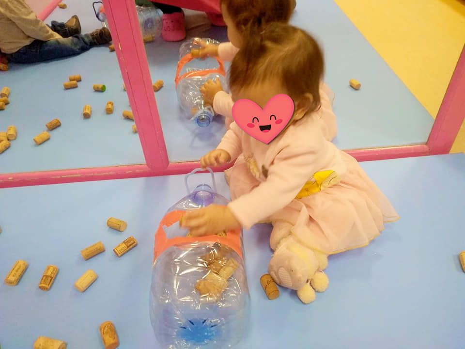 Dos bebés juegan con botellas y corchos frente a un espejo.