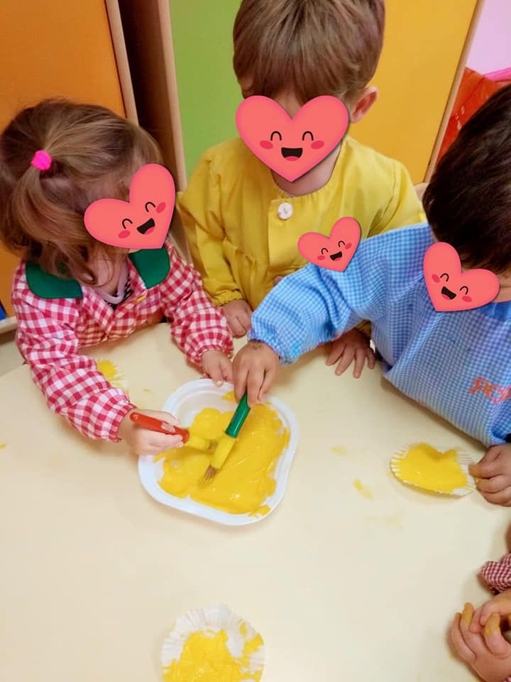 Un grupo de niños está sentado en una mesa jugando con pintura amarilla.