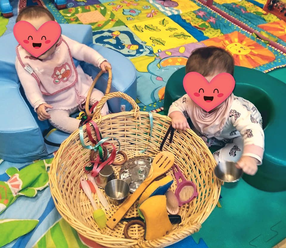 Dos bebés con corazones en sus caras están sentados junto a una canasta de juguetes.