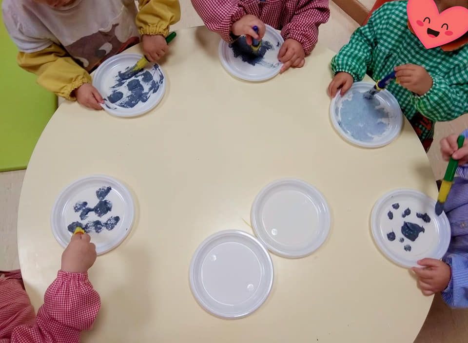 Un grupo de niños está sentado alrededor de una mesa pintando en platos de papel.