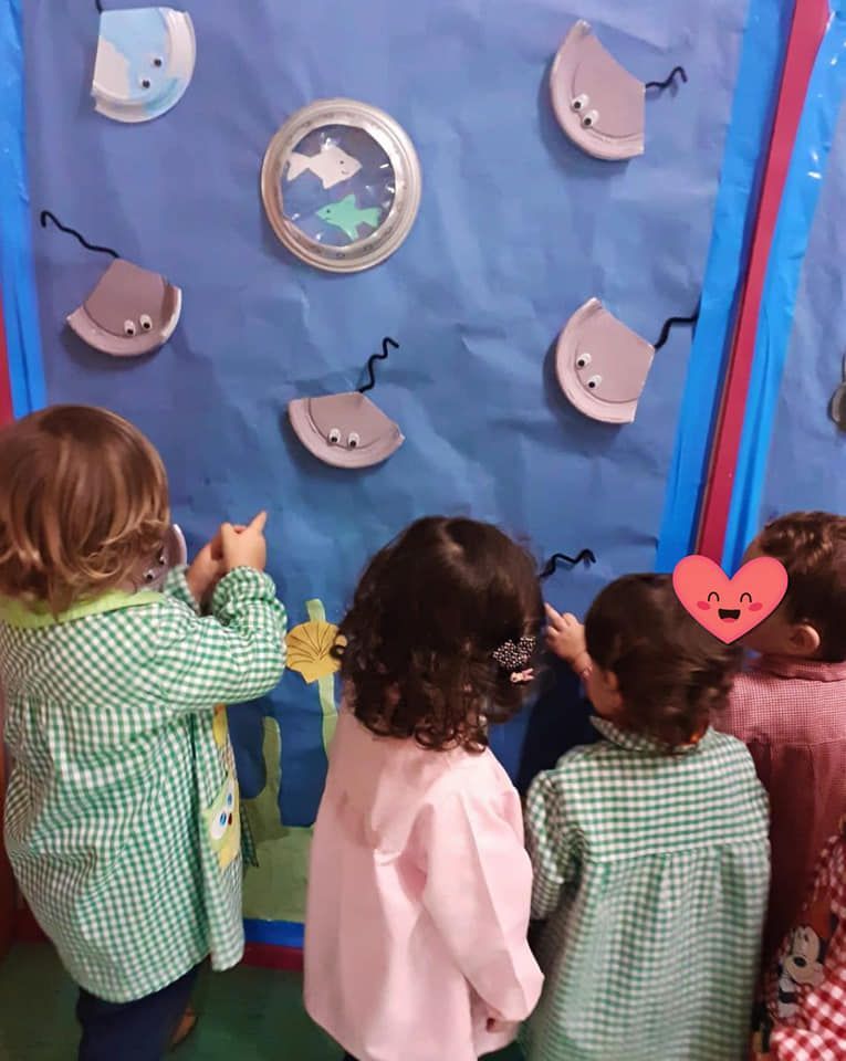 Un grupo de niños mira una pecera hecha con platos de papel.