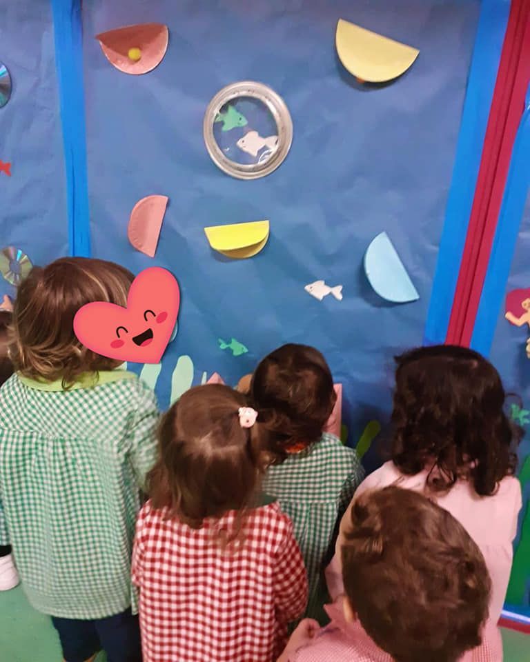 Un grupo de niños mira una pared con peces de papel.