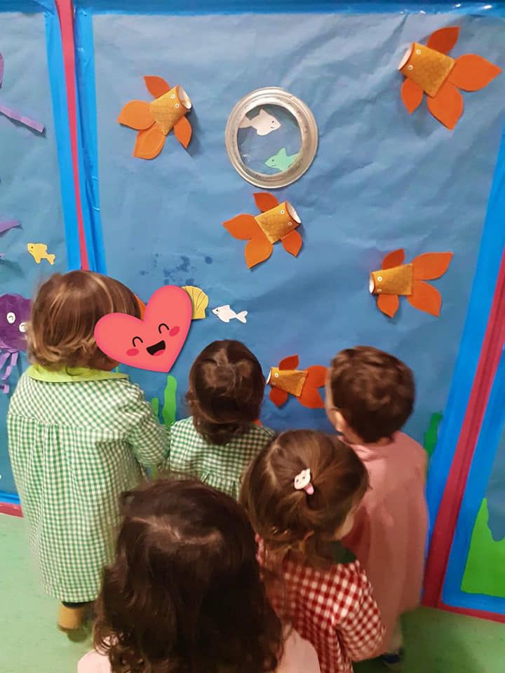 Un grupo de niños está mirando una pecera hecha con vasos de papel.