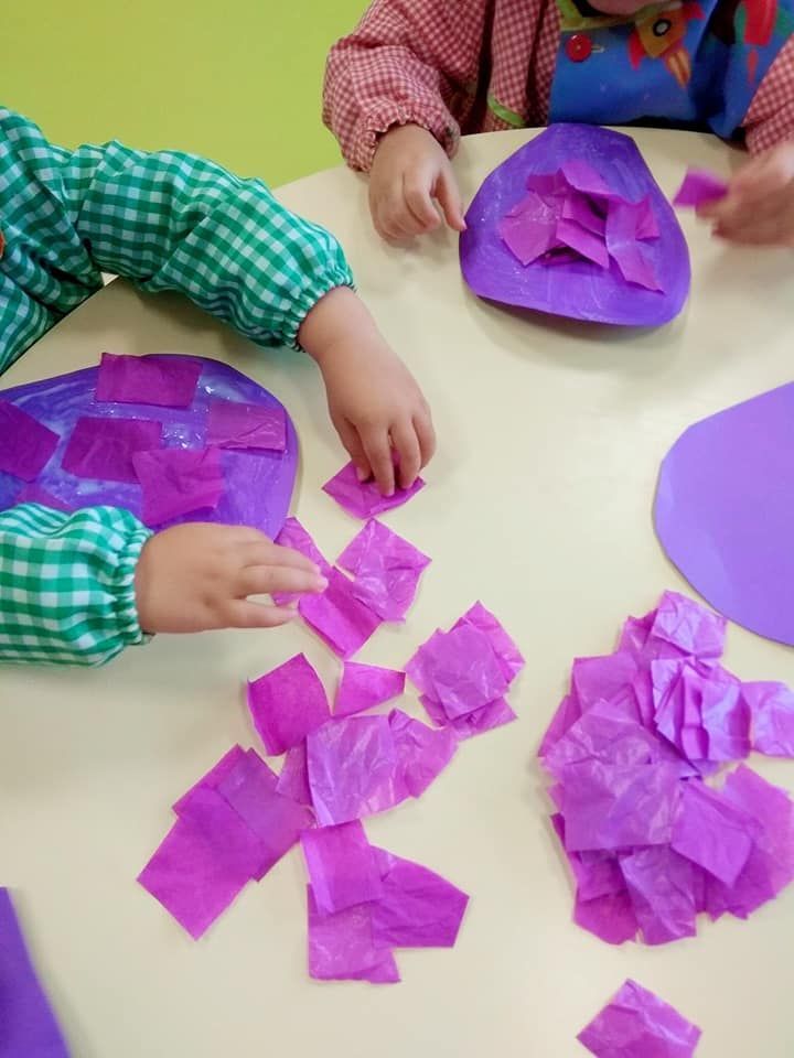 Dos niños están jugando con papel de seda morado sobre una mesa.