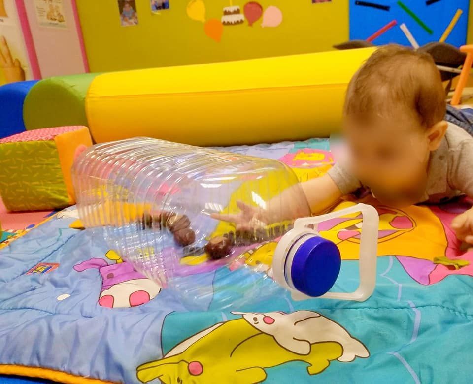 Un bebé está jugando con una botella de plástico sobre una colchoneta.