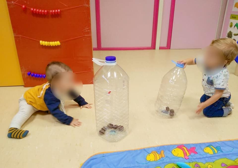 Dos bebés están jugando con botellas de plástico en el suelo.