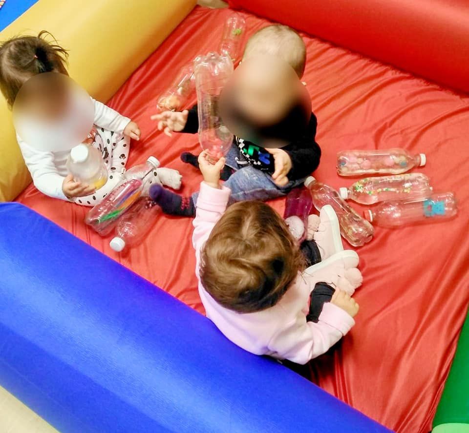 Tres niños juegan con botellas de plástico en una piscina inflable