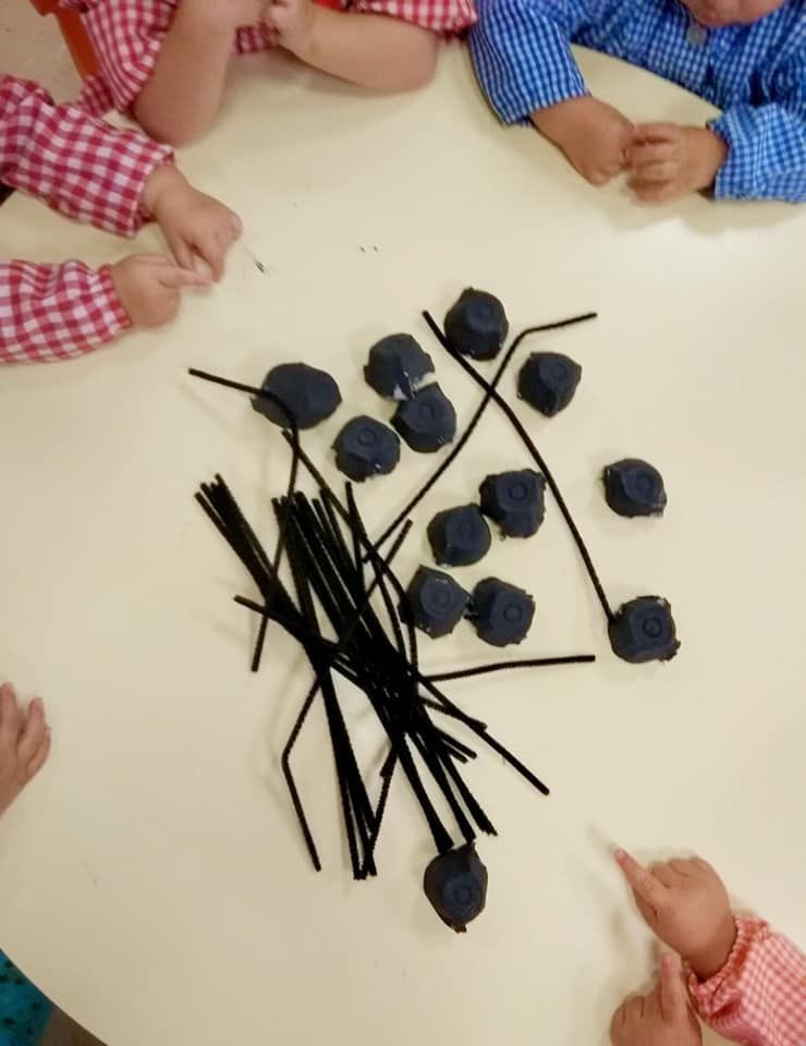 Un grupo de niños están sentados alrededor de una mesa con un montón de objetos negros sobre ella.