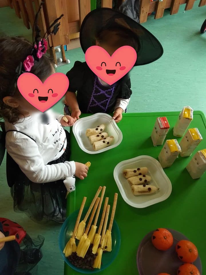 Dos niños disfrazados de brujas están sentados en una mesa con platos de comida.