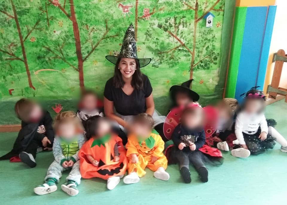Una mujer con un sombrero de bruja está sentada junto a un grupo de niños vestidos con disfraces de Halloween.