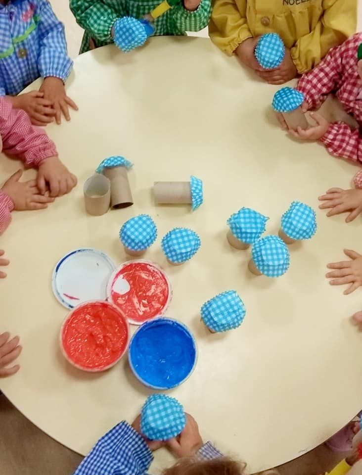 Un grupo de niños están sentados alrededor de una mesa con cuencos de pintura.