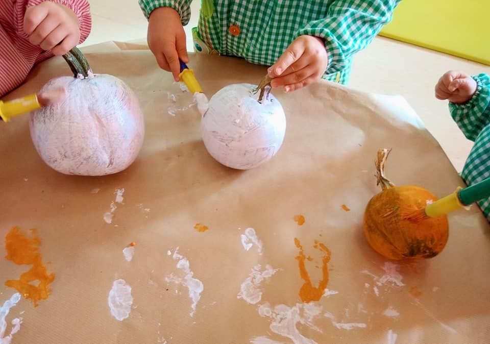 Dos niños están pintando calabazas en una mesa con pinceles.