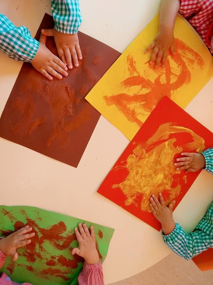 Un grupo de niños están sentados alrededor de una mesa jugando con pinturas.