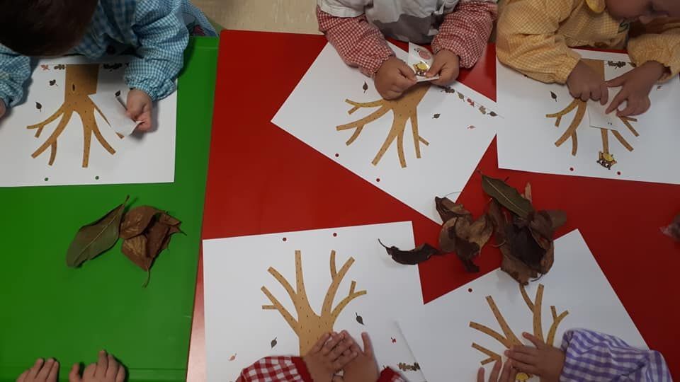Un grupo de niños están sentados en una mesa haciendo un árbol con sus manos.