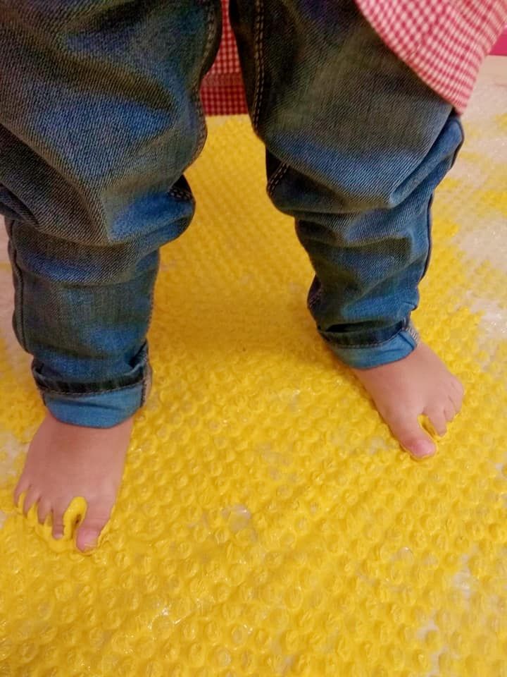 Los pies de un bebé están parados sobre una alfombra amarilla.