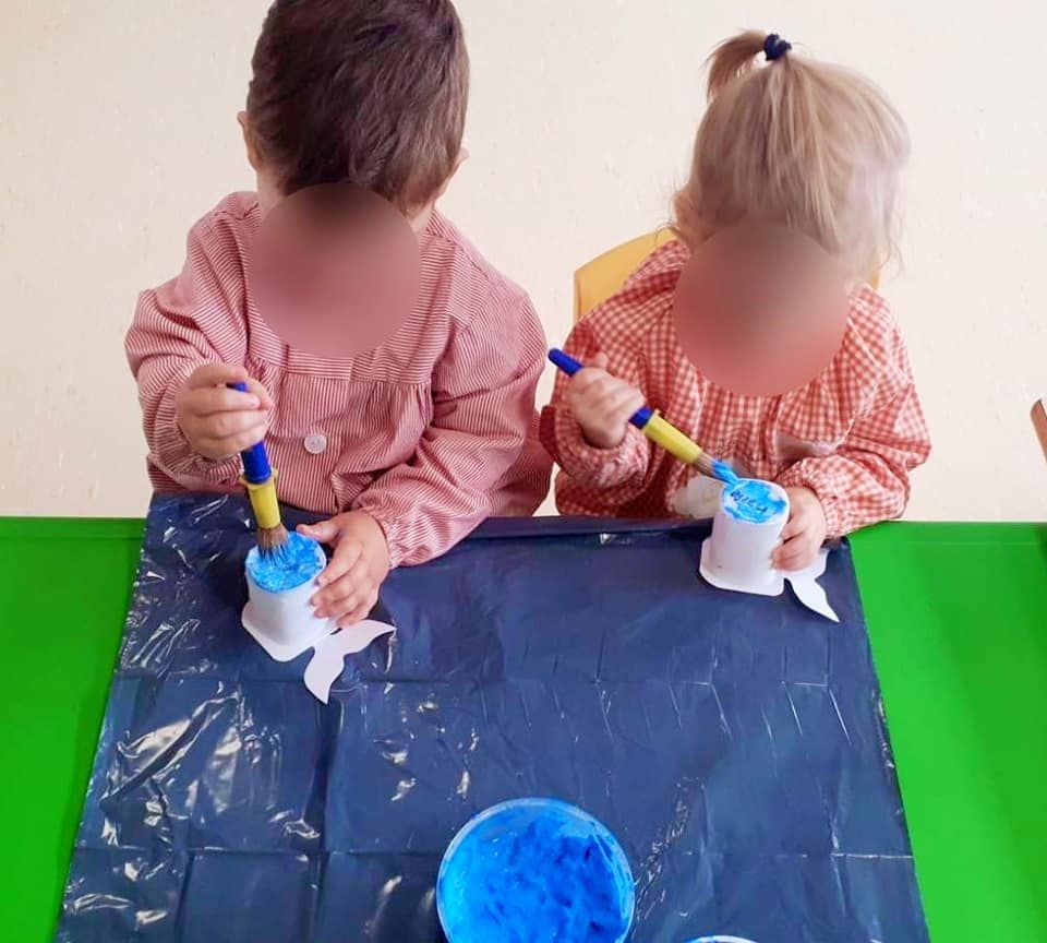 Dos niños están sentados en una mesa con pintura azul y pinceles.