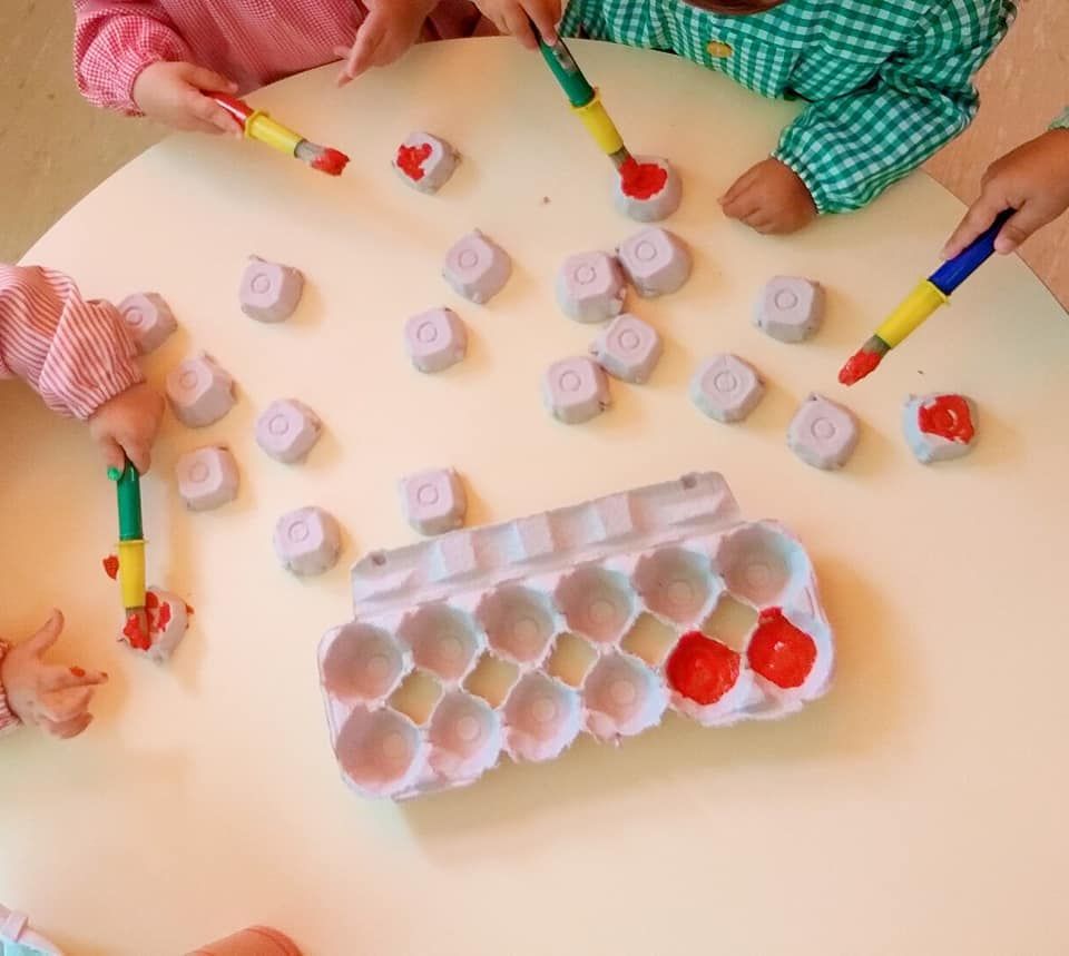 Los niños juegan con cartones de huevos y pinceles sobre una mesa.
