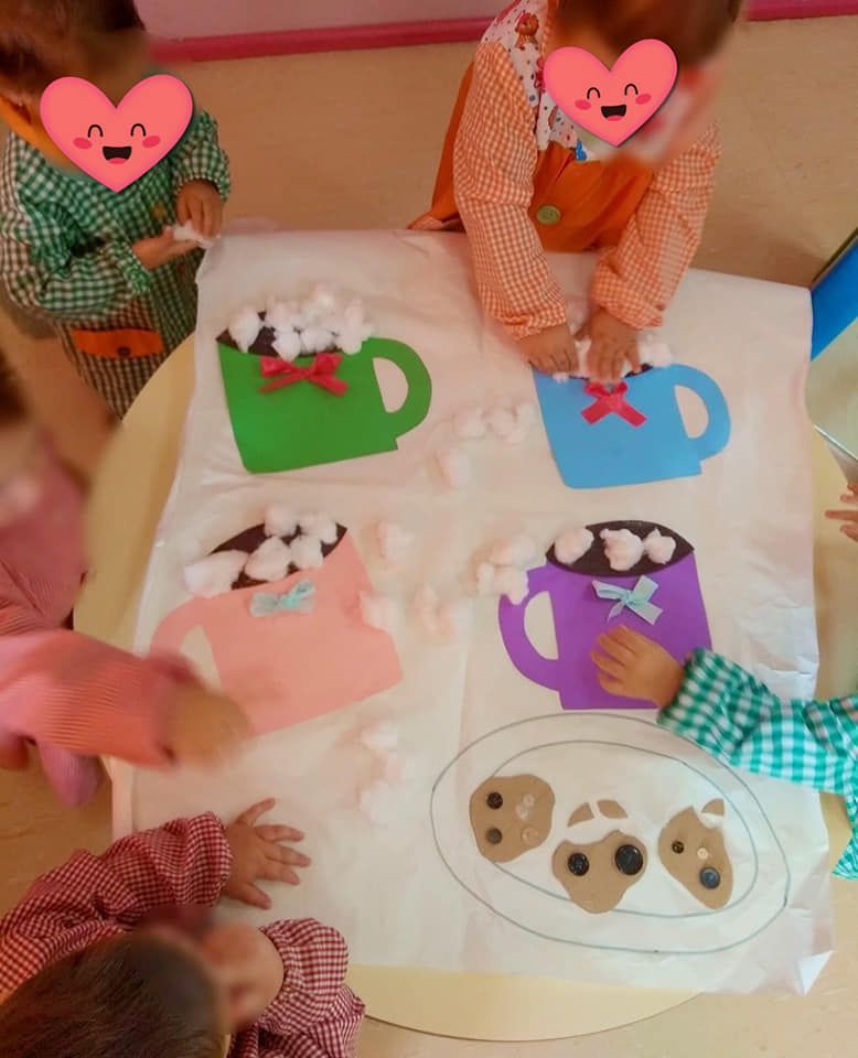Un grupo de niños están sentados alrededor de una mesa con tazas de chocolate caliente y malvaviscos.