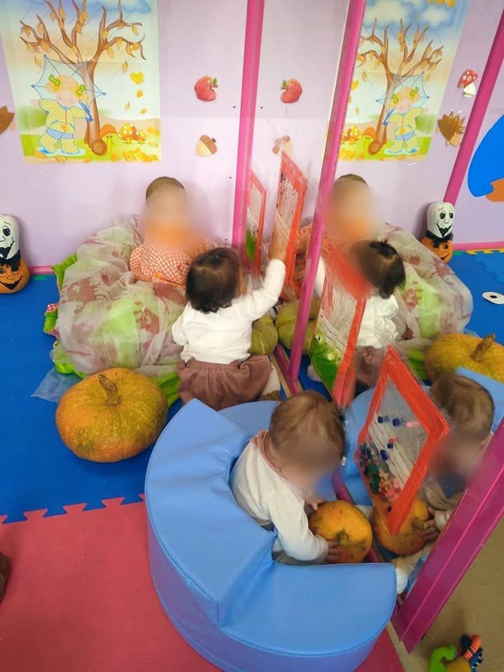 Un grupo de bebés está jugando en una habitación con calabazas y un espejo.