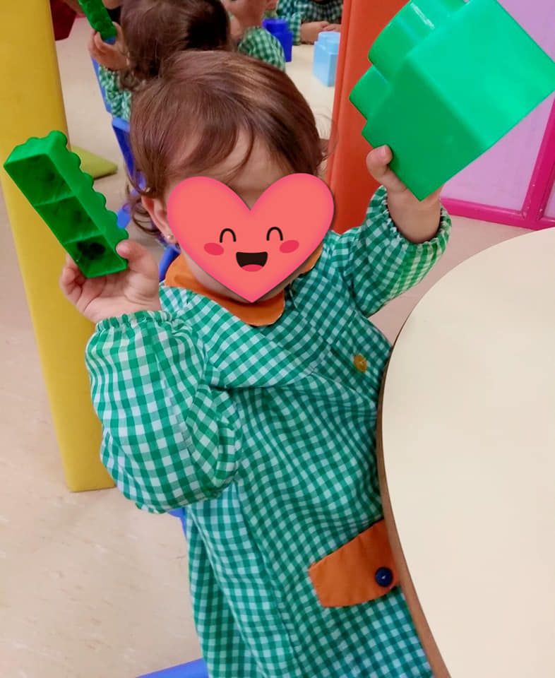 Una niña con un corazón en la cara sostiene un bloque verde.