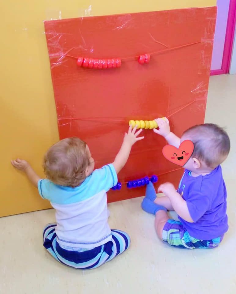 Dos niños pequeños están jugando con un tablero rojo con cuentas.