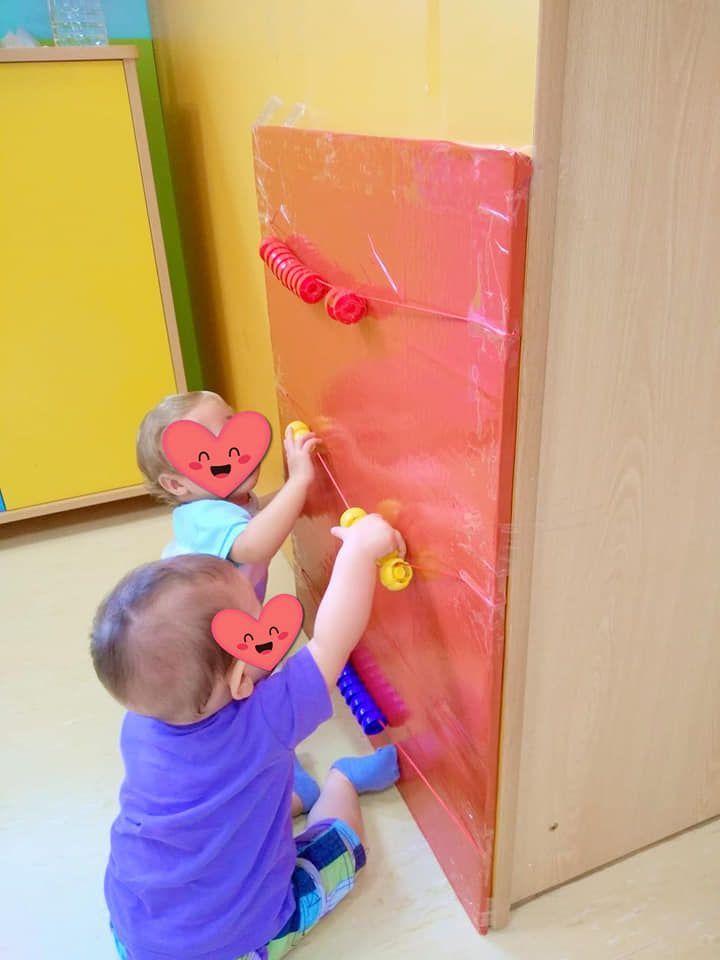 Dos bebés están jugando con juguetes en una pared.