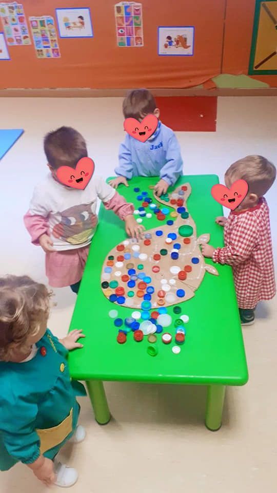 Un grupo de niños está jugando con tapas de botellas en una mesa verde.