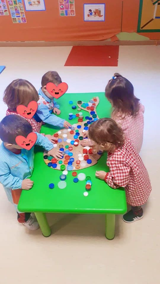 Un grupo de niños está sentado alrededor de una mesa verde jugando con botones.