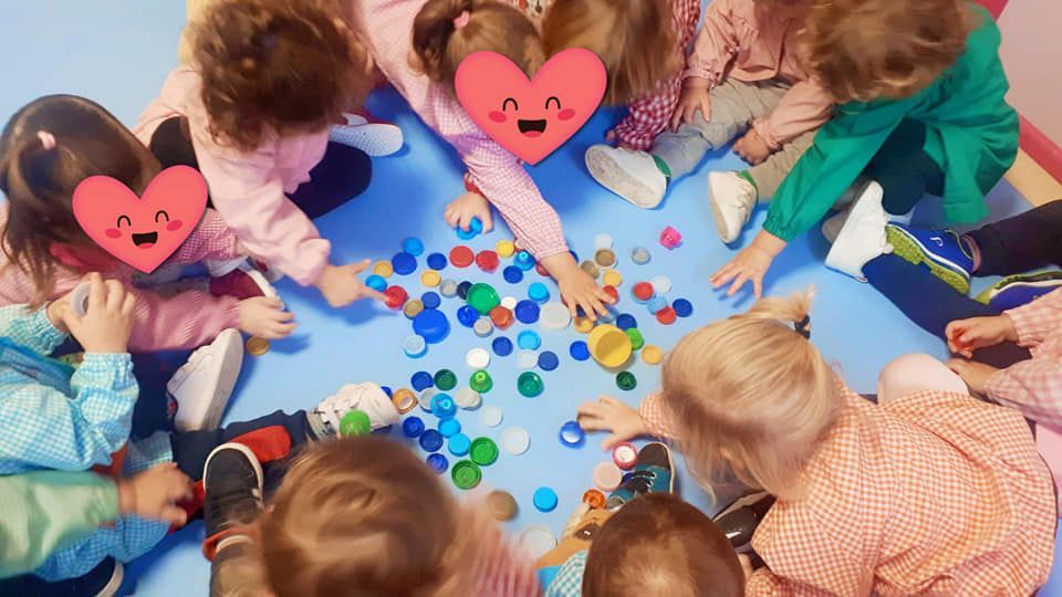 Un grupo de niños está sentado en círculo jugando con tapas de botellas de plástico.