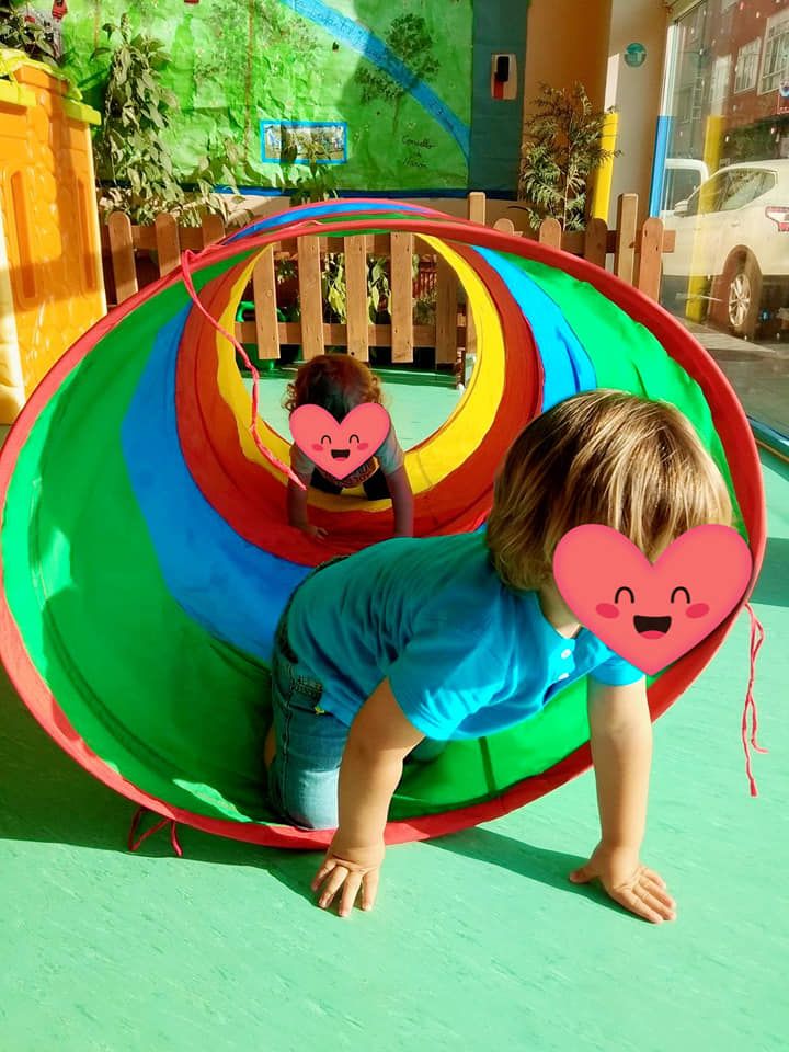Dos niños gatean por un túnel colorido.