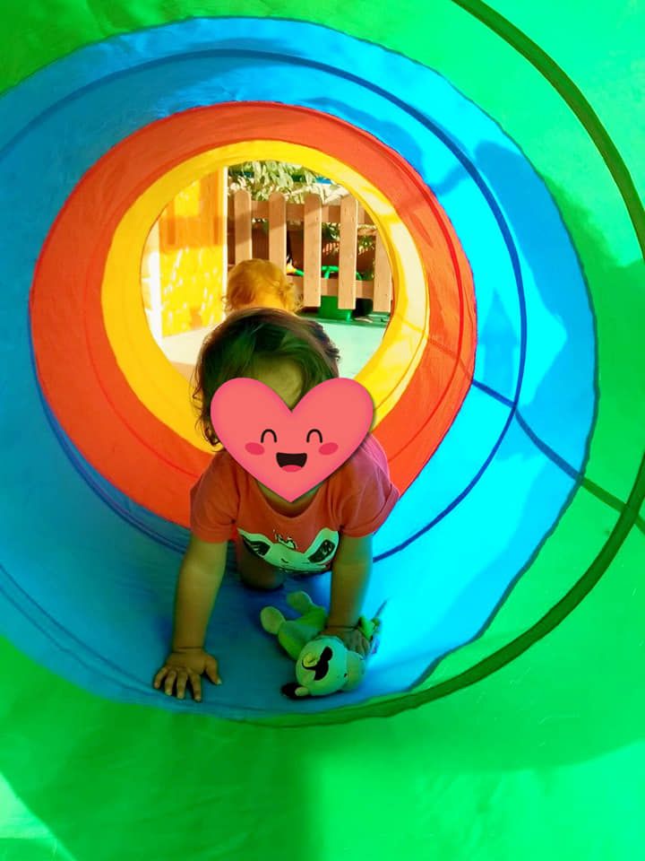 Una niña gatea por un túnel colorido.