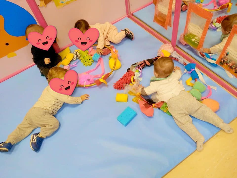 Un grupo de bebés están acostados sobre una alfombra azul jugando con juguetes.