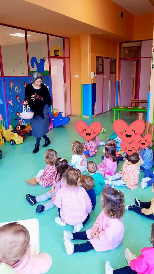 Una mujer está parada frente a un grupo de niños sentados en el suelo.