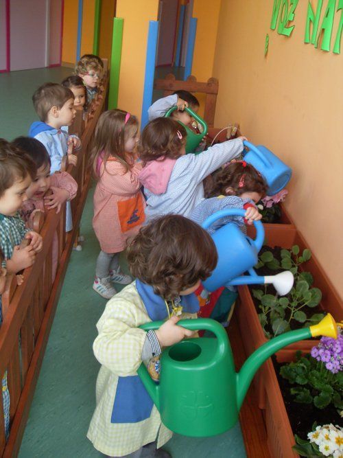 Un grupo de niños riegan las plantas con regaderas.